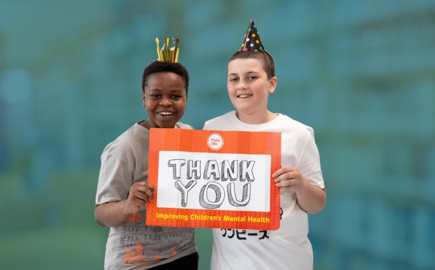 Two young boys wearing party hats and holding a Place2 sign that says 'Thank you'