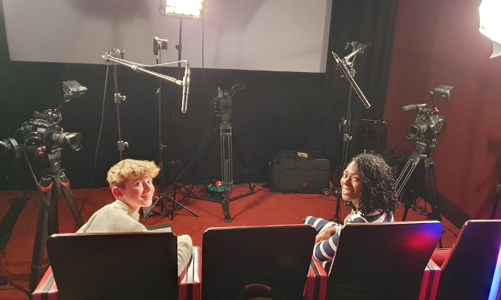 Young BAFTA Presenter Tristan and broadcaster Shanequa Paris. They are sitting on chairs with recording equipment like cameras and microphones around them