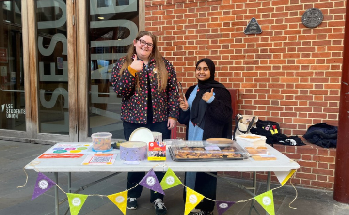Two university students standing by their bake sale outside a university building