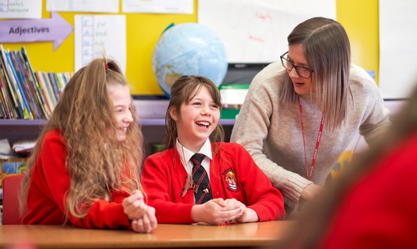 Teacher with two primary age female students, laughing at desk Teacher with two primary age female students, laughing at desk