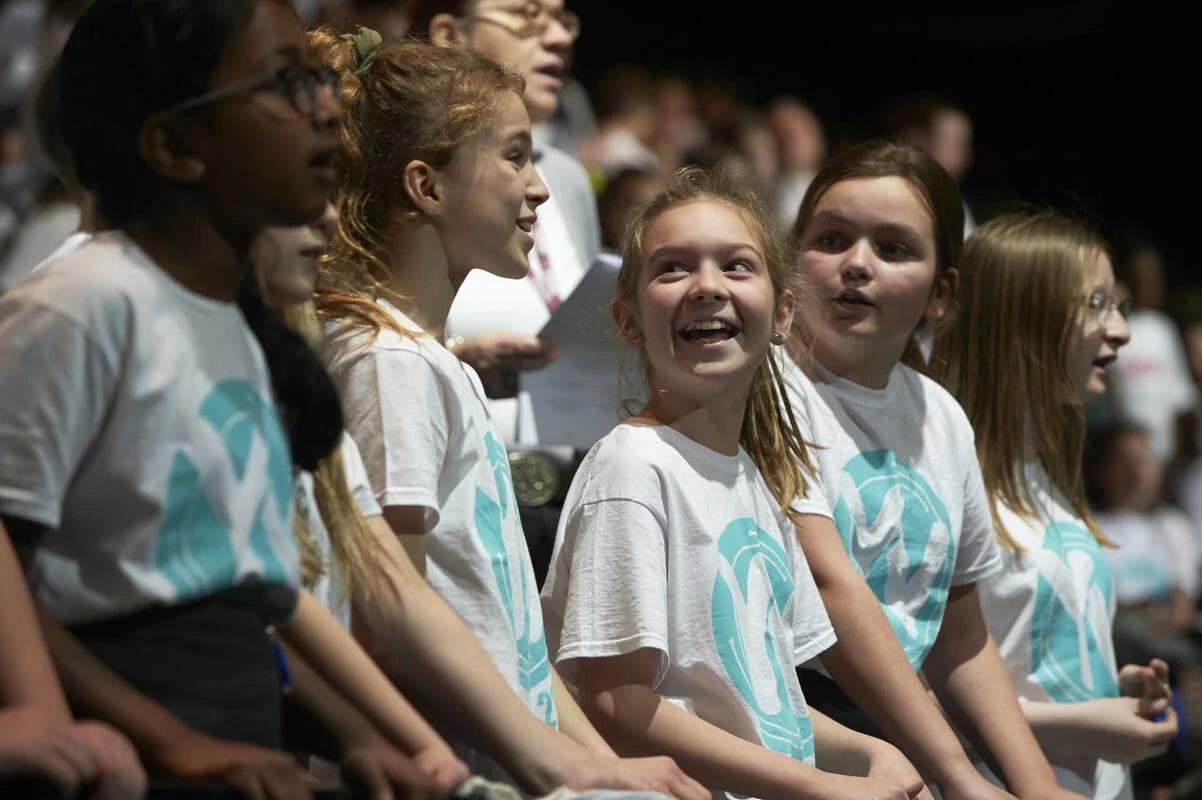 School pupils taking part in a Young Voices concert. They are talking and laughing with each other.