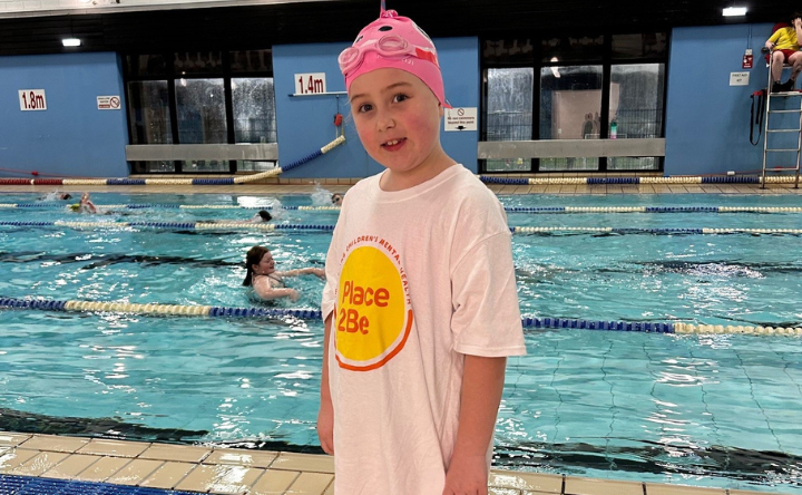 Young girl wearing a Place2Be T-shirt. She is standing next to a swimming pool.