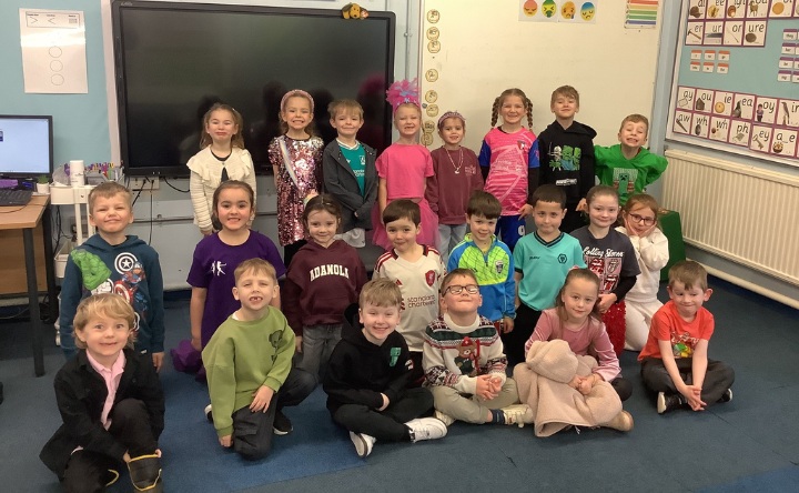 A class of 22 primary aged pupils sitting and standing in a classroom. They are all dressed in non-uniform clothes or costumes and smiling at the camera.