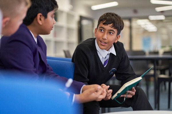 Three students sitting in a classroom, talking in a group about a piece of work