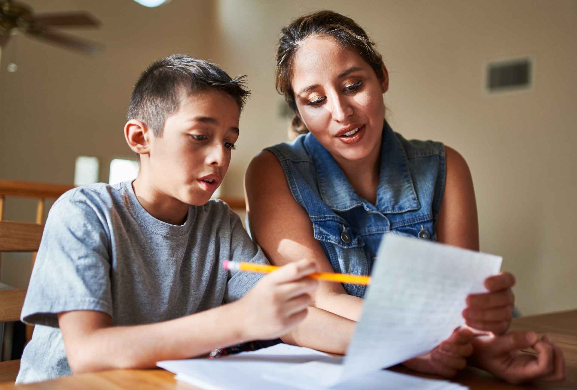 A young teenage boy sitting at home with his mum writing