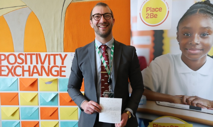 Will Stone is holding a sign saying 'I'm supporting Place2Be's Children's Mental Health Week' and smiling