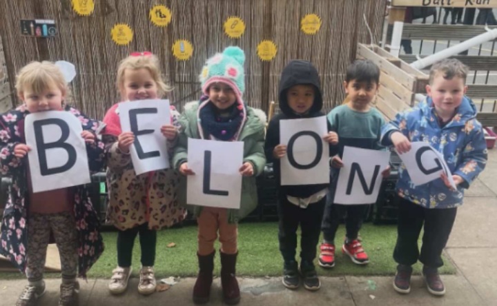 6 young children, each holding up a piece of paper with a letter on it. The letters spell out 'Belong' in line with the theme of Children's Mental Health Week 2026, This is My Place