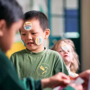 A primary-aged boy in a classroom with Children's Mental Health Week stickers on his face