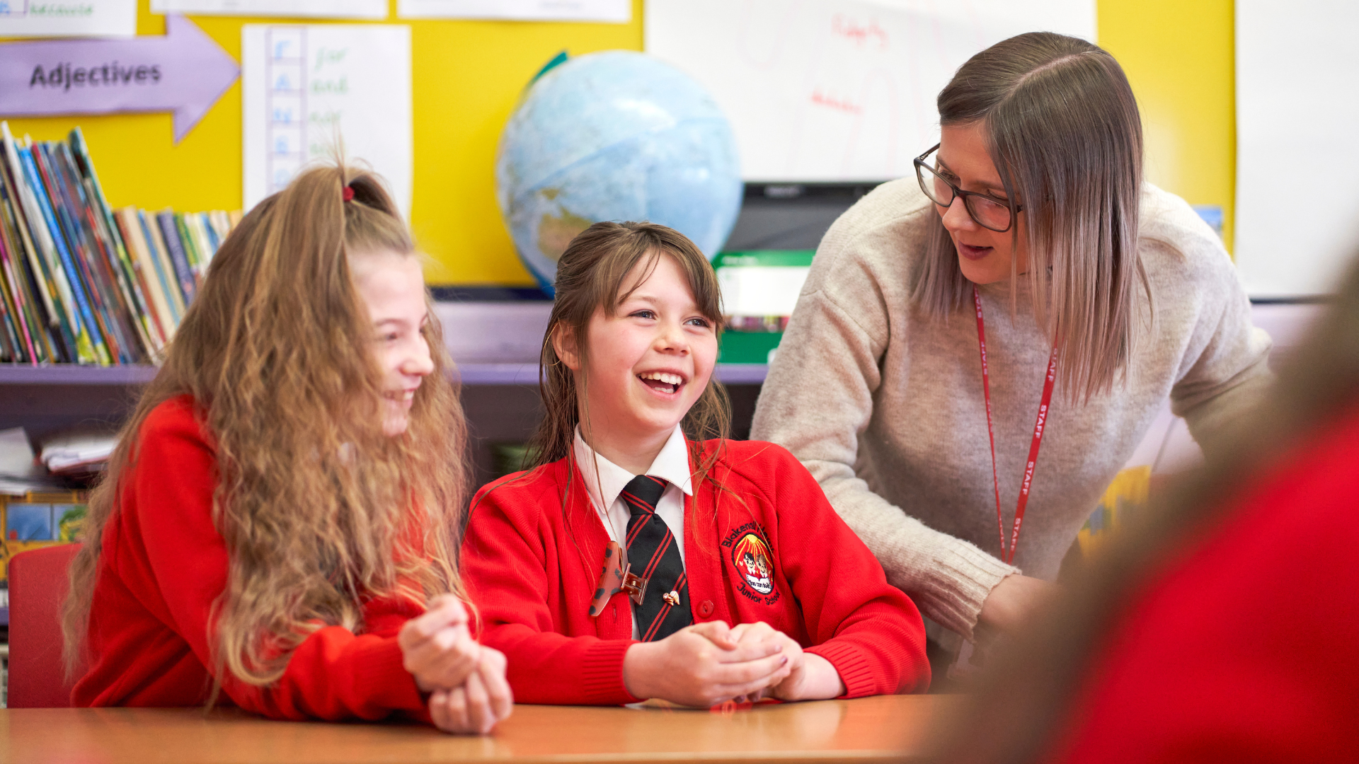 Teacher with two primary age female students, laughing at desk