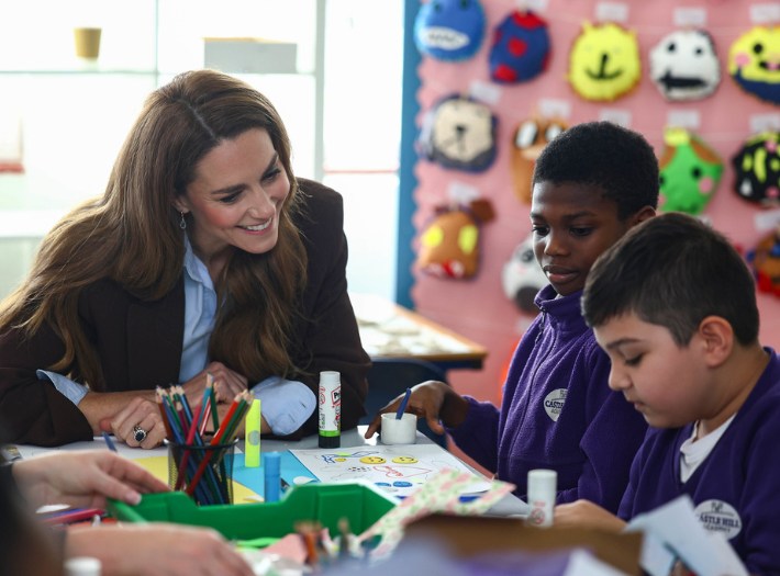 The Princess of Wales sitting at a table with pupils, looking at their artwork and smiling