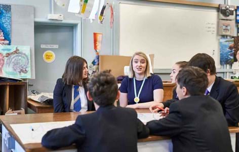 Group of secondary school students talking round a table with a member of staff